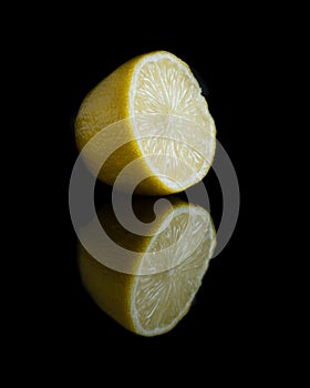 Cut yellow lemon in black background with reflection