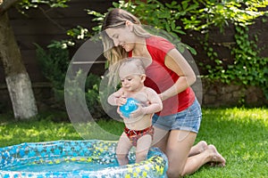 Cute 10 months old baby boy enjoying swimming in inflatable pool at house backyard