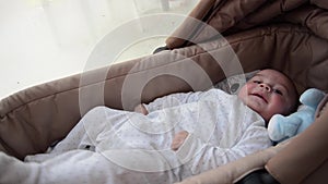 Cute 3 months old baby boy making funny faces in baby carry cot