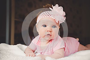 Cute 3 months old baby girl in pink lying down on a white bed at home. Big open eyes. Infant napping in bed. Healthy