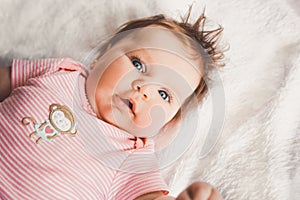 Cute 3 months old baby girl in pink lying down on a white bed at home looking at camera. Big open eyes. Infant napping