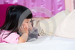 Cute 4 year old Asian girl lying prone on the mattress. Little kid holding her chin. Touchy child, bad mood, unhappy children.