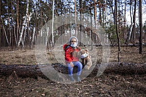 A cute 6-7 years old girl in red coat wearing respirator mask playing with toy teddy bear alone