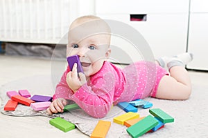 Cute 6 month baby girl plays wooden multicolored meccano at home