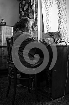 Cute 80 plus year old senior woman using vintage sewing machine. Black and white image of adorable elderly woman sewing clothes.