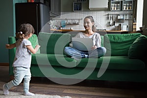 Cute active girl playing while mother using laptop at home