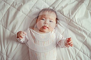 cute adorable Asian mixed race baby girl four months old lying on bed in bedroom looking in camera.