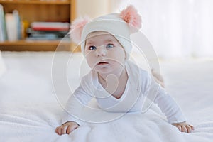 Cute adorable baby child with warm white and pink hat with cute bobbles. Happy baby girl learning crawl and looking at