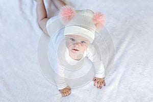 Cute adorable baby child with warm white and pink hat with cute bobbles. Happy baby girl learning crawl and looking at