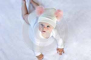 Cute adorable baby child with warm white and pink hat with cute bobbles. Happy baby girl learning crawl and looking at