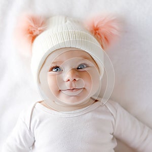 Cute adorable baby child with warm white and pink hat with cute bobbles. Happy baby girl on white background and looking