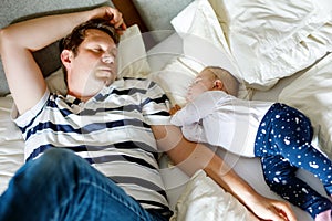 Cute adorable baby girl of 6 months and her father sleeping peaceful in bed at home