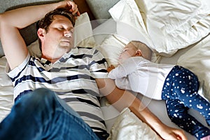 Cute adorable baby girl of 6 months and her father sleeping peaceful in bed at home