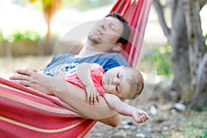 Cute adorable baby girl of 6 months and her father sleeping peaceful in hammock in outdoor garden