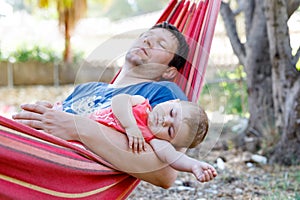 Cute adorable baby girl of 6 months and her father sleeping peaceful in hammock in outdoor garden. Closeup of beautiful