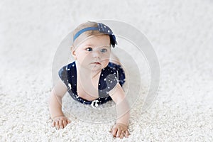 Cute adorable baby girl in blue clothes and headband. little child looking at the camera and crawling. Baby learning