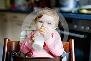 Cute adorable baby girl holding nursing bottle and drinking formula milk. First food for babies. New born child, sitting
