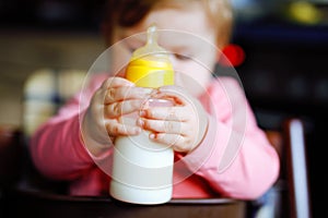 Cute adorable baby girl holding nursing bottle and drinking formula milk. First food for babies. New born child, sitting