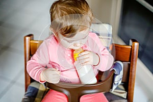 Cute adorable baby girl holding nursing bottle and drinking formula milk. First food for babies. New born child, sitting