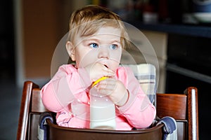 Cute adorable baby girl holding nursing bottle and drinking formula milk. First food for babies. New born child, sitting