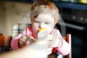 Cute adorable baby girl holding nursing bottle and drinking formula milk. First food for babies. New born child, sitting