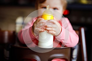 Cute adorable baby girl holding nursing bottle and drinking formula milk. First food for babies. New born child, sitting