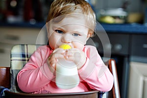 Cute adorable baby girl holding nursing bottle and drinking formula milk. First food for babies. New born child, sitting