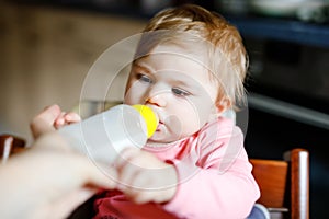 Cute adorable baby girl holding nursing bottle and drinking formula milk. First food for babies. New born child, sitting