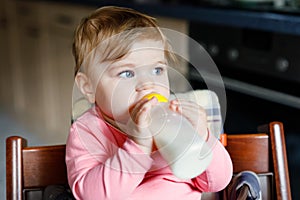 Cute adorable baby girl holding nursing bottle and drinking formula milk. First food for babies. New born child, sitting