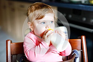 Cute adorable baby girl holding nursing bottle and drinking formula milk. First food for babies. New born child, sitting