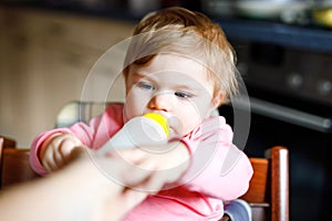 Cute adorable baby girl holding nursing bottle and drinking formula milk. First food for babies. New born child, sitting in chair