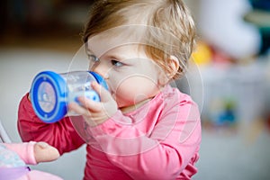 Cute adorable baby girl holding nursing bottle and drinking formula milk or water. First food for babies. Healthy babies