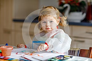 Cute adorable baby girl learning painting with water colors. Little toddler child drawing at home, using colorful