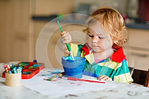 Cute adorable baby girl learning painting with water colors. Little toddler child drawing at home, using colorful