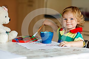 Cute adorable baby girl learning painting with water colors. Little toddler child drawing at home, using colorful