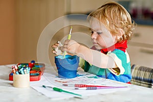 Cute adorable baby girl learning painting with water colors. Little toddler child drawing at home, using colorful