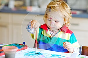 Cute adorable baby girl learning painting with water colors. Little toddler child drawing at home, using colorful