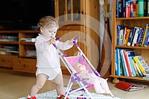 Cute adorable baby girl making first steps with doll carriage.