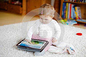 Cute adorable baby girl watching cartoons on tablet pc. Todder child at home touching on screen and playing educational