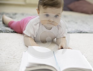A cute adorable baby reads a book on the carpet. Early development and education