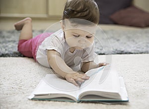 A cute adorable baby turns pages in a book on the carpet
