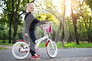 Cute adorable beautiful caucasian little blond girl enjoy riding white small bicycle by path in green summer city park forest or