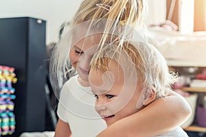 Cute adorable blond caucaian little sister hugging her toddler brother.couple of cheerful sibling playing indoor. Cute