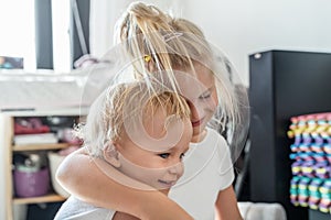 Cute adorable blond caucaian little sister hugging her toddler brother.couple of cheerful sibling playing indoor. Cute girl and