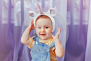 Cute adorable Caucasian baby girl wearing unicorn headband with horn, ears. Pretty funny child kid with head hair fairy tale