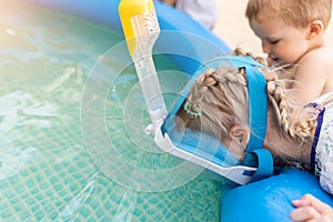 Cute adorable caucasian blond little girl making experiment try diving in pool with full face snorkel mask in inflatable