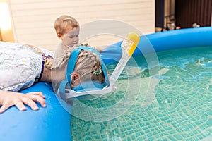 Cute adorable caucasian blond little girl making experiment try diving in pool with full face snorkel mask in inflatable