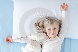Cute adorable caucasian blond little toddler kid girl lying in bed on white pillow. Adorable sweet happy smiling child stretching