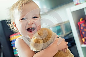 Cute adorable caucasian blond toddler boy having fun, laughing and hugging soft puppy toy indoors. Cheerful child playing with