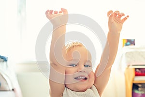 Cute adorable caucasian blond toddler boy having fun, laughing and rising hands up indoors. Cheerful child playing with positive